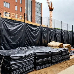 Tapume de lona plástica preta em canteiro de obras protegendo material de construção contra chuva
